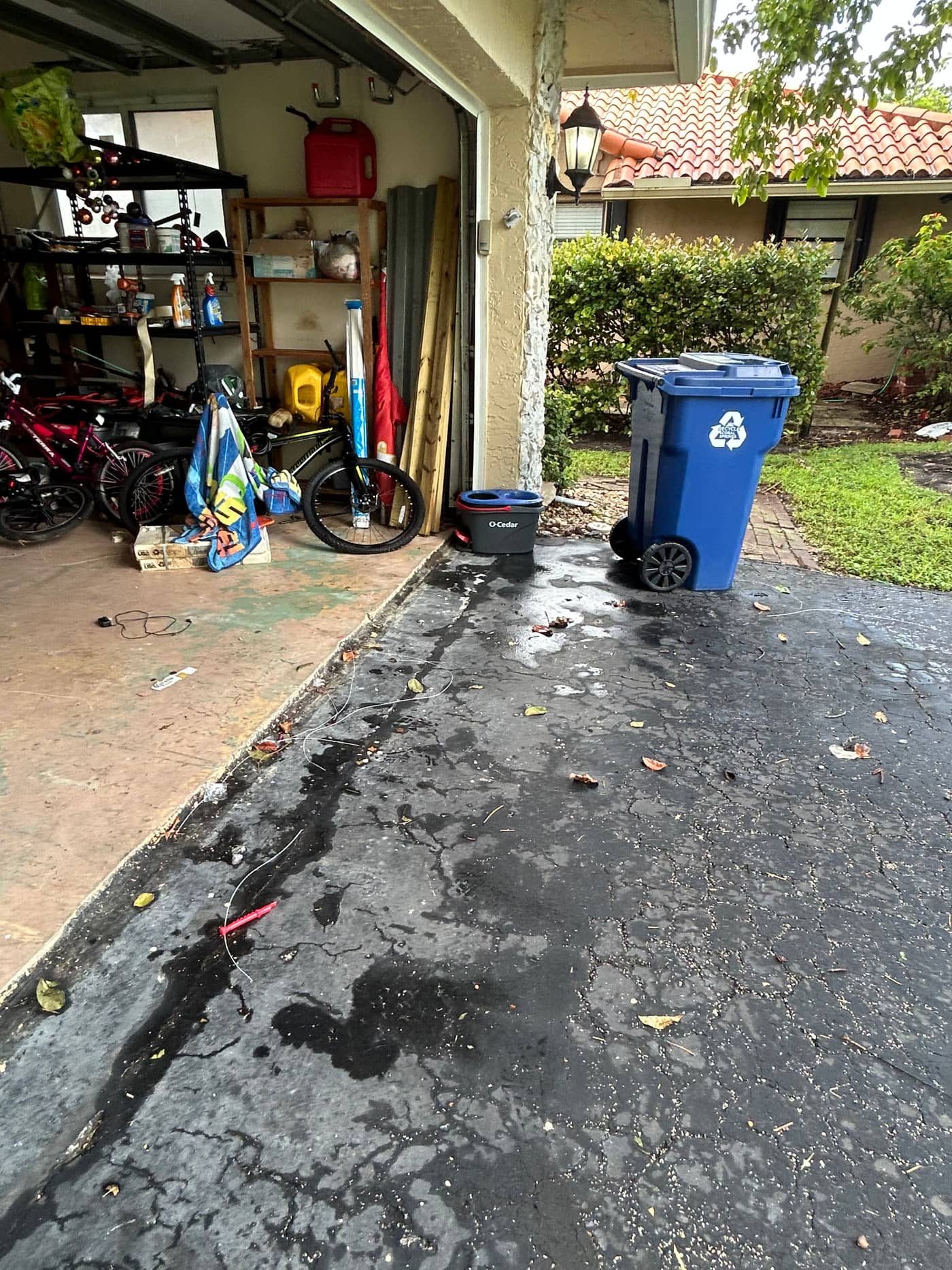 The same driveway wet and clear, with the garage behind it showing bikes, shelving and a recycling bin