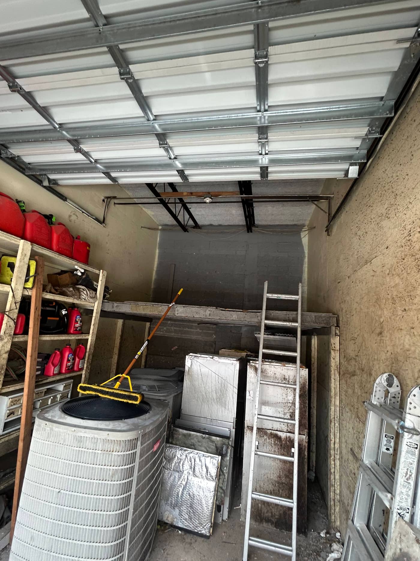 The same garage with the pile gone, showing bare floor, a shelving rack, a ladder and the air handler that stayed