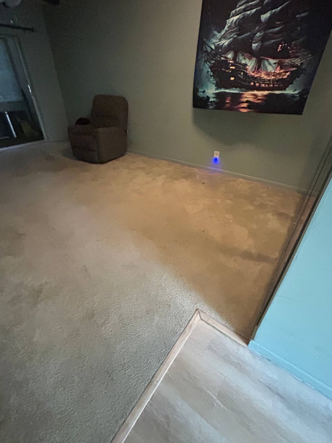 The same living room with the furniture gone, showing open carpet and a single armchair left against the far wall