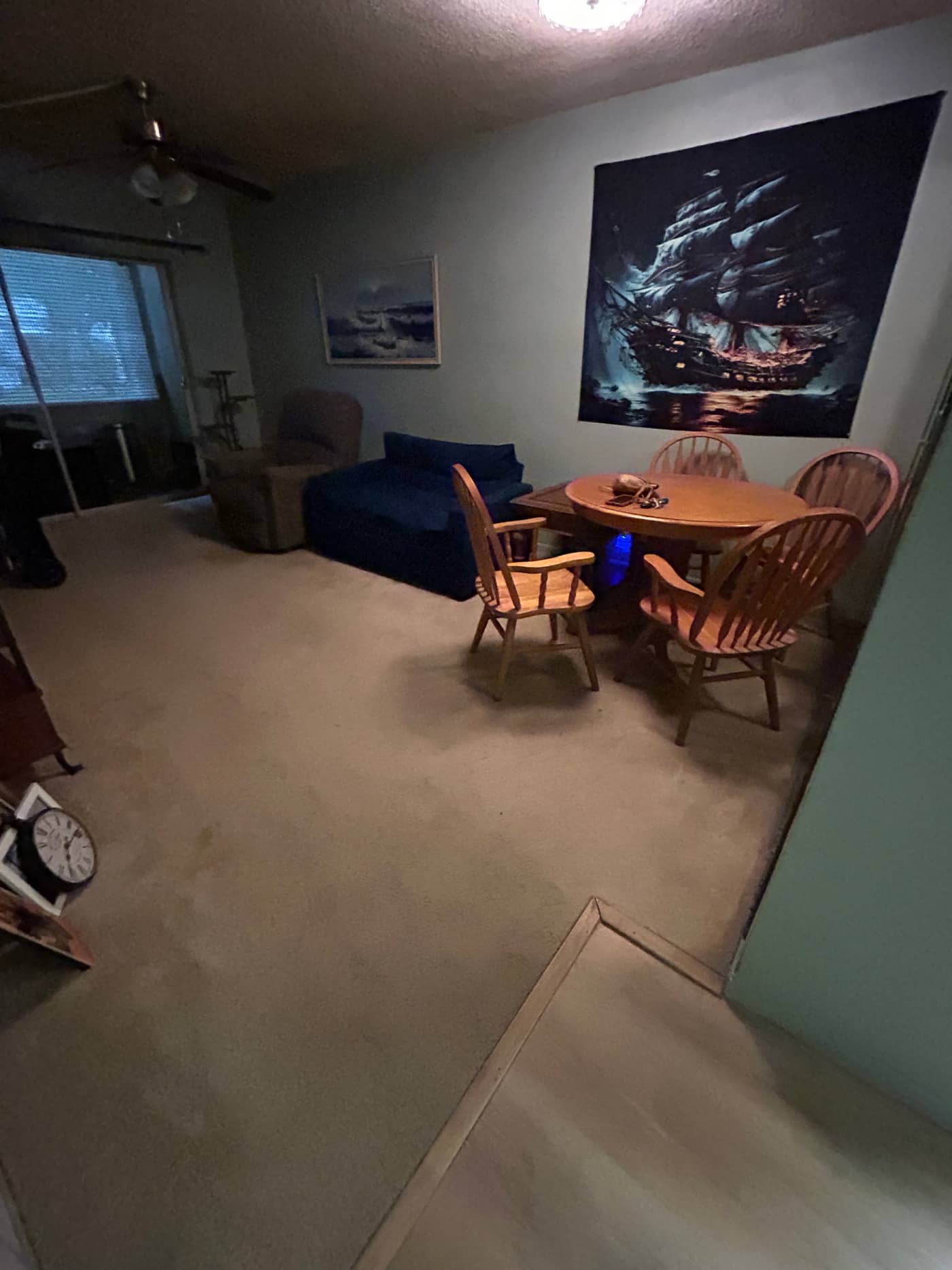 A living room with a blue sofa, a round wooden dining table and four chairs, an armchair and a framed picture leaning against the wall