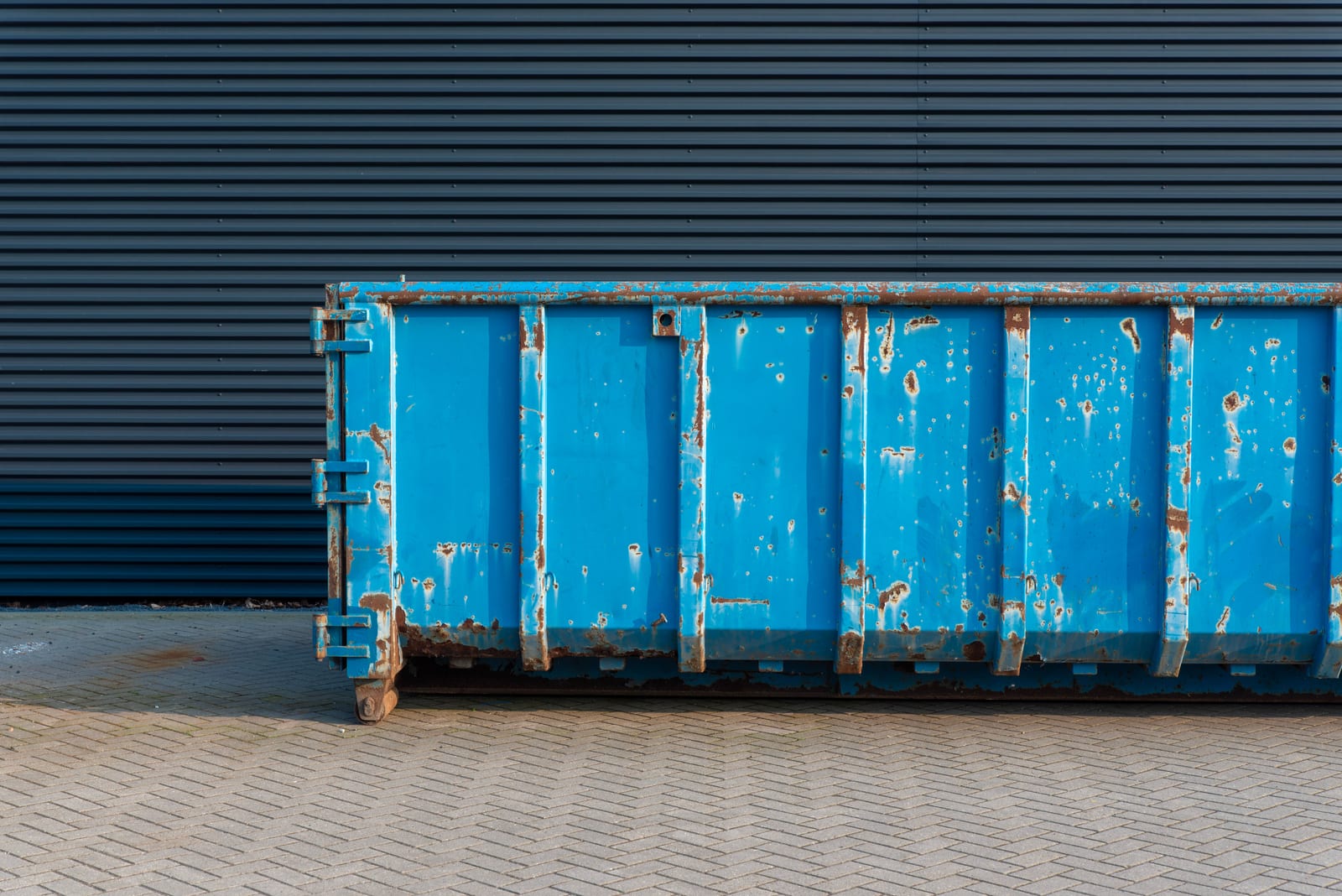 A blue roll-off container parked against a wall, the alternative to having a crew carry it out