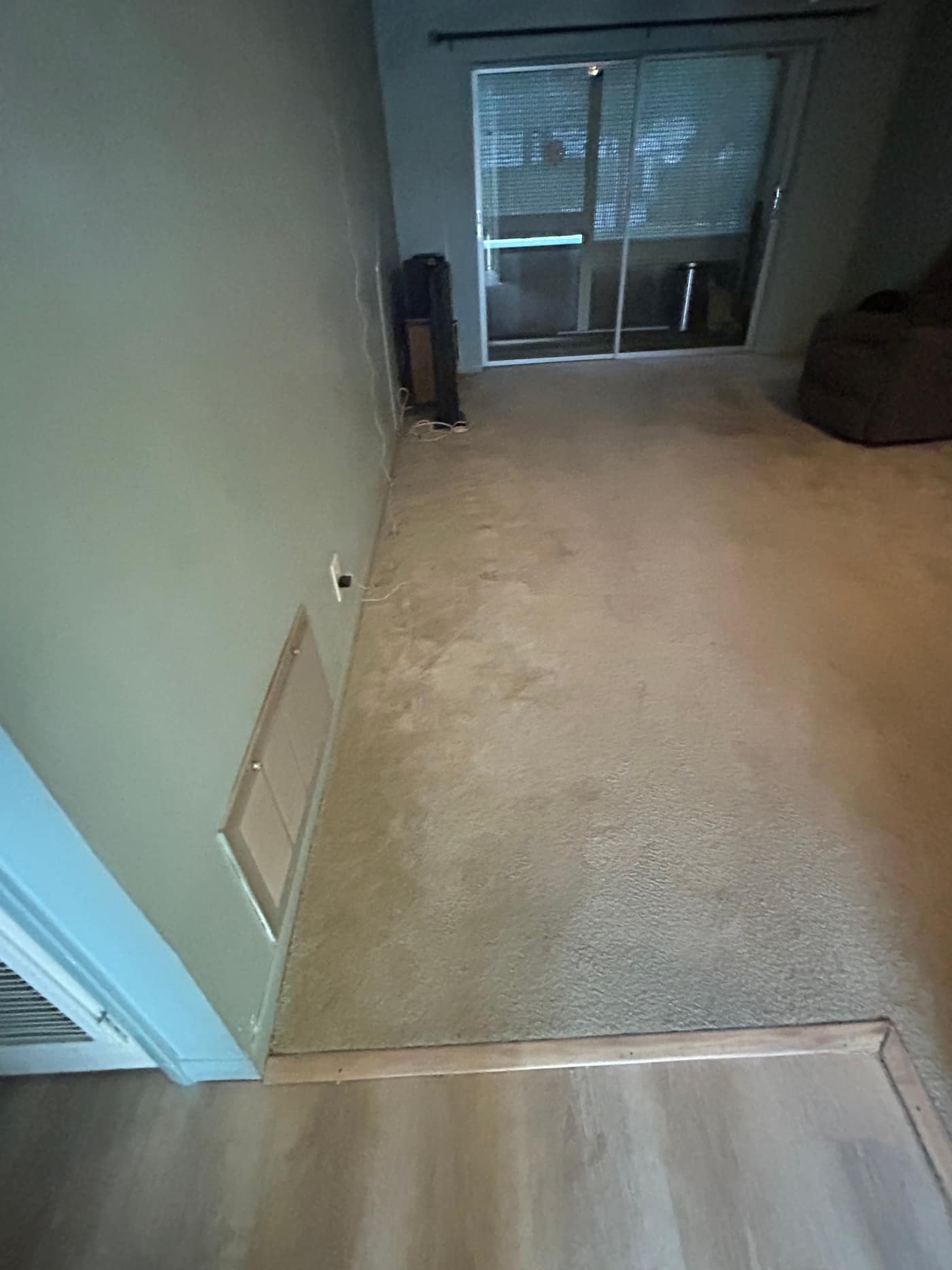 The same apartment cleared to open carpet running to the sliding patio door, with only a small cabinet and a beanbag left in the room